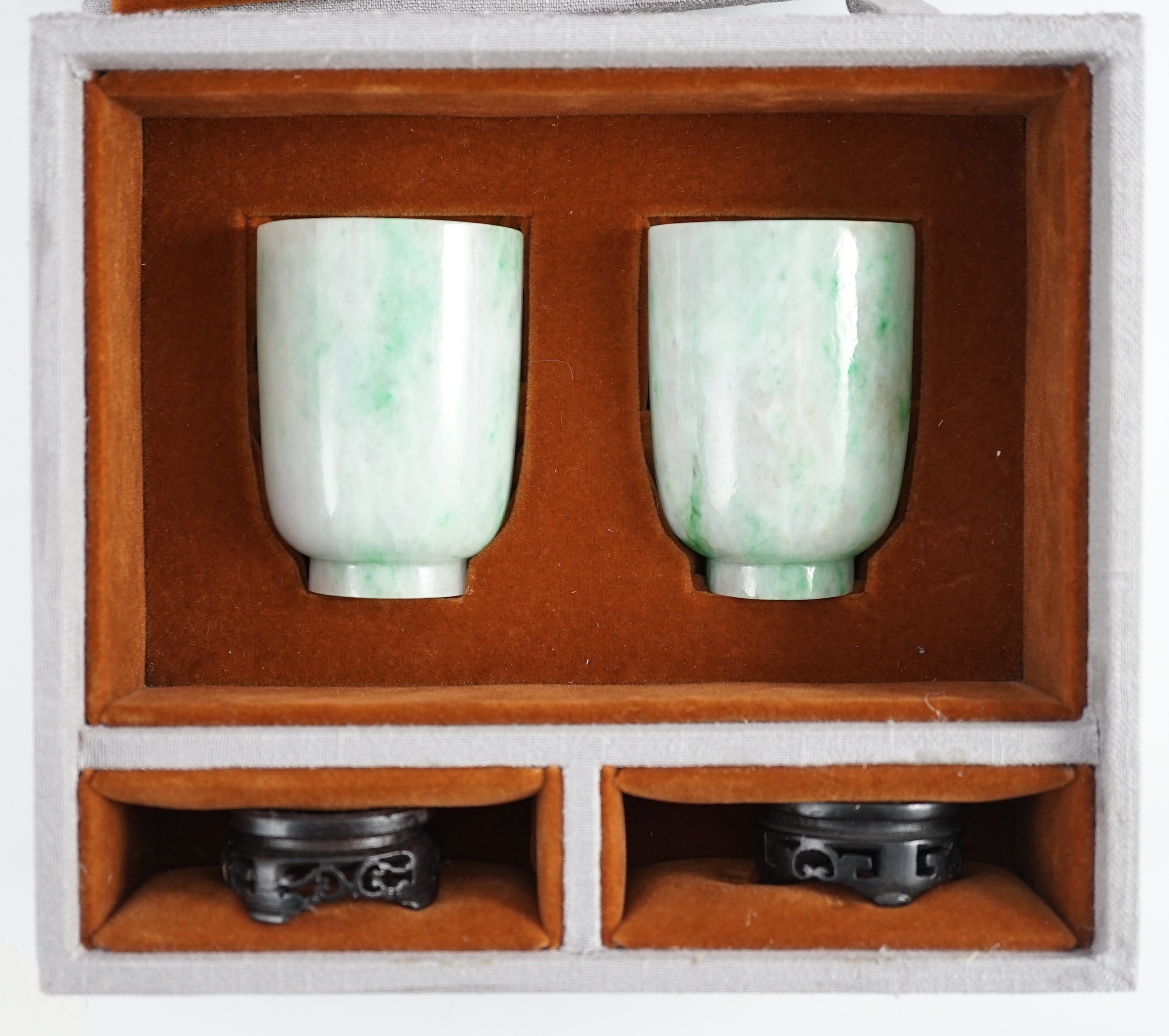 A pair of Chinese jadeite cups, 6.2cm high, wood stands, fitted box